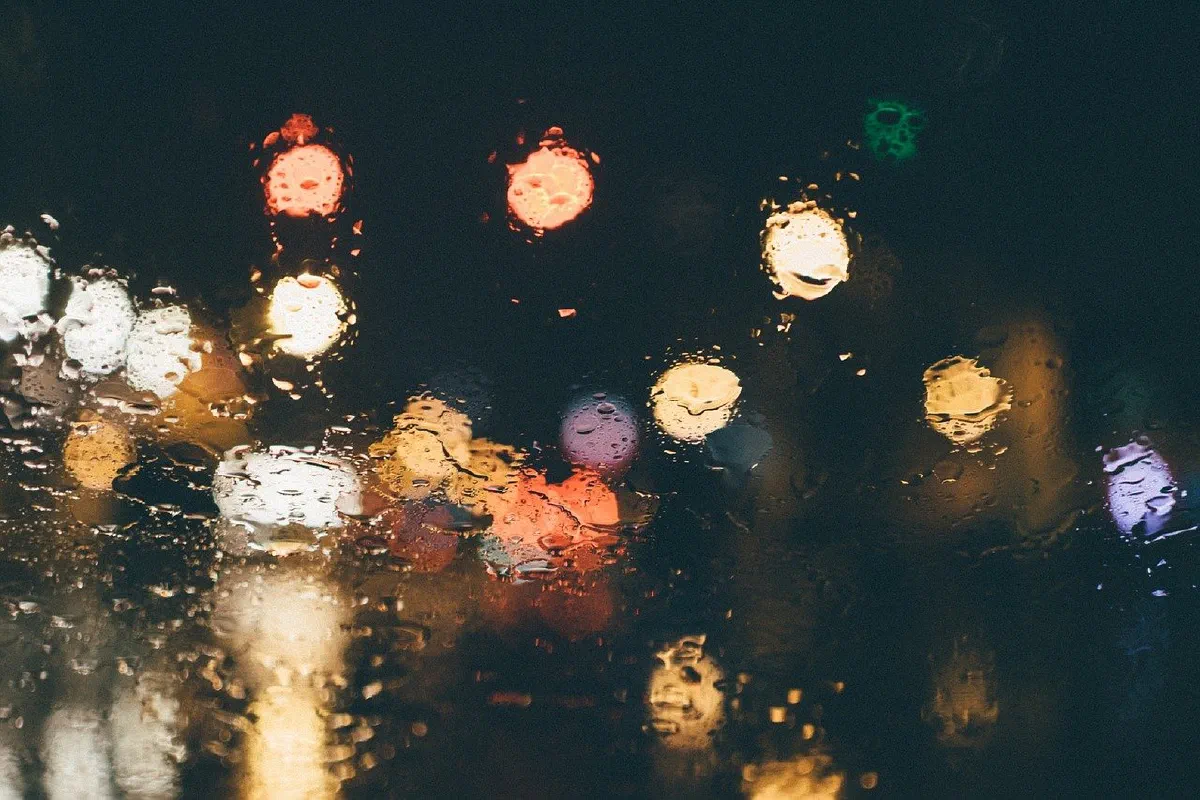 Verregnete Fensterscheibe bei Nacht mit unscharfen, bunten Lichtern und Ampeln im Hintergrund